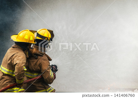 Two firefighters extinguishing a large fire with a hose Two firefighters extinguishing a large fire with a hose 141406760