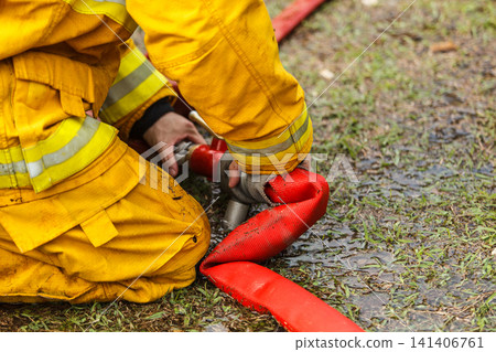 Firefighter connecting a red water hose on the ground 141406761