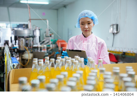 Quality control specialist examining juice bottle on production line Quality control specialist examining juice bottle on production line 141406804