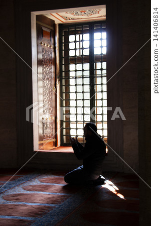 Silhouette of person praying near ornate window in sunlight Silhouette of person praying near ornate window in sunlight 141406814