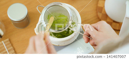 Person sifting vibrant green matcha powder during a tea preparation session Person sifting vibrant green matcha powder during a tea preparation session 141407007