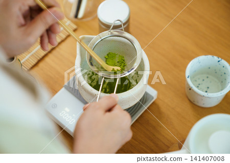 Person sifting vibrant green matcha powder during a tea preparation session Person sifting vibrant green matcha powder during a tea preparation session 141407008