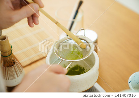 Person sifting vibrant green matcha powder during a tea preparation session 141407010