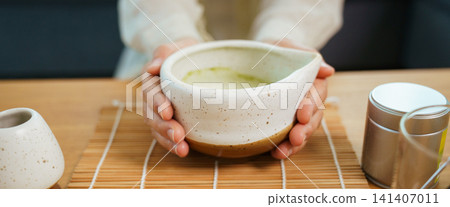 Close up of hands holding traditional ceramic bowl of matcha green tea Close up of hands holding traditional ceramic bowl of matcha green tea 141407011