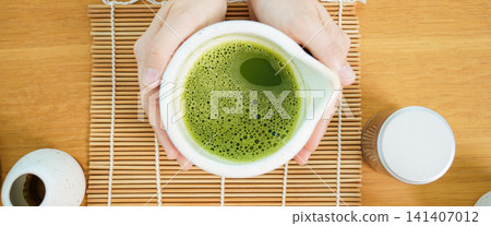 Top view of hands holding a ceramic bowl of foamy matcha green tea Top view of hands holding a ceramic bowl of foamy matcha green tea 141407012