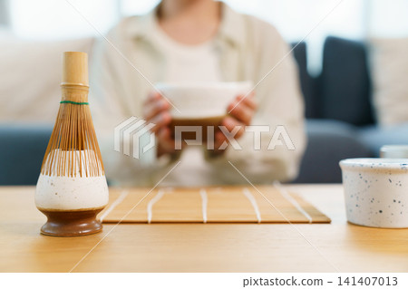 Traditional Japanese bamboo whisk on ceramic holder with blurred person holding matcha bowl Traditional Japanese bamboo whisk on ceramic holder with blurred person holding matcha bowl 141407013