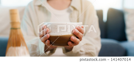 Close up of hands holding traditional ceramic bowl of matcha green tea Close up of hands holding traditional ceramic bowl of matcha green tea 141407014