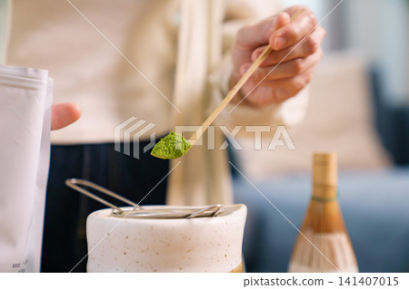 Close up of hand using traditional bamboo scoop to measure matcha powder over strainer Close up of hand using traditional bamboo scoop to measure matcha powder over strainer 141407015