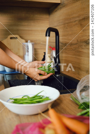 Hands hold green beans under running water in kitchen sink before meal preparation Hands hold green beans under running water in kitchen sink before meal preparation 141407106