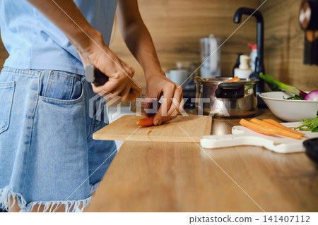 Close-up view of unrecognizable woman slicing fresh carrot lengthwise Close-up view of unrecognizable woman slicing fresh carrot lengthwise 141407112