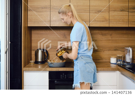 Woman pours boiled baby potatoes from saucepan into roasting pan for baking Woman pours boiled baby potatoes from saucepan into roasting pan for baking 141407136