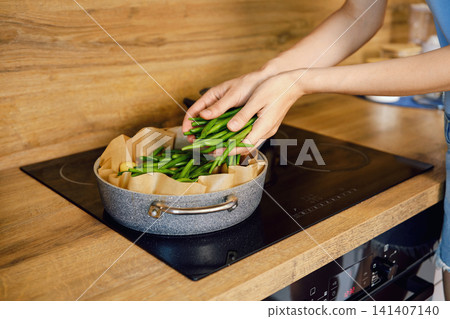 Hands place fresh green beans onto parchment paper in large roasting pan on stovetop Hands place fresh green beans onto parchment paper in large roasting pan on stovetop 141407140