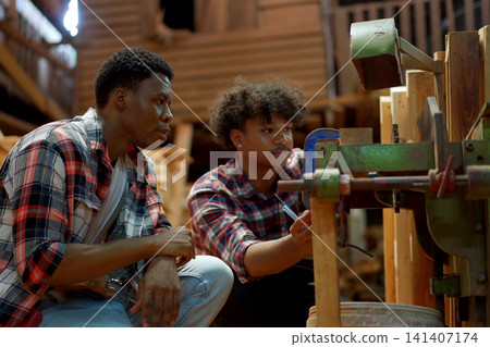Two carpenters inspecting a machine in a woodworking workshop Two carpenters inspecting a machine in a woodworking workshop 141407174