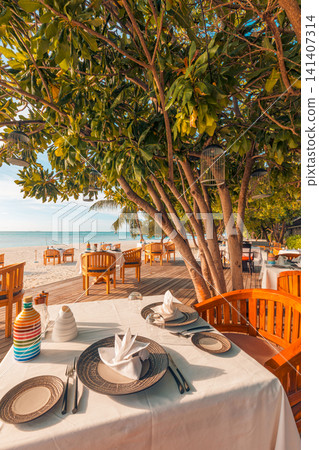 Gorgeous table setting beachfront restaurant framed by trees over ocean tropical resort dining terrace. Perfect travel hospitality dining outdoors service. Luxury romantic honeymoon warm scenic 141407314