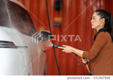 woman washing car with water hose in a self-service car wash station woman washing car with water hose in a self-service car wash station 141407996