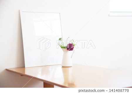 木桌上擺放著紫色的花朵、白色的花瓶和一個空相框。 木桌上擺放著紫色的花朵、白色的花瓶和一個空相框。 141408770