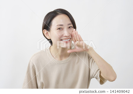 A woman with her hand to her mouth calls out to someone against a white background. A woman with her hand to her mouth calls out to someone against a white background. 141409042