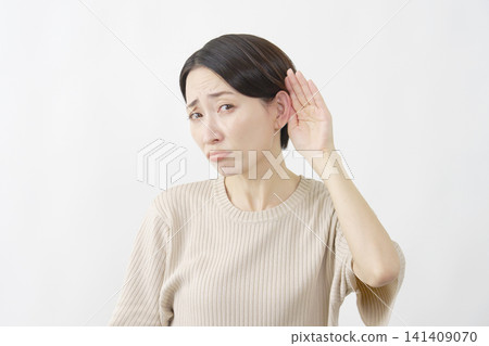 A woman with her hand to her ear asks for clarification against a white background. A woman with her hand to her ear asks for clarification against a white background. 141409070