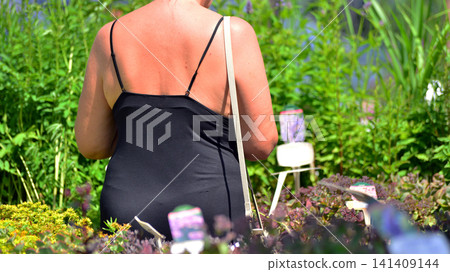 A woman in a black summer dress chooses flowers for her summer garden at a garden center. A woman in a black summer dress chooses flowers for her summer garden at a garden center. 141409144