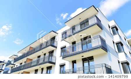 Contemporary urban apartment block with protruding balconies, white and grey facade contrast and reflective windows under a bright sky. Contemporary urban apartment block with protruding balconies, white and grey facade contrast and reflective windows under a bright sky. 141409799