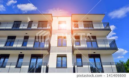 Contemporary urban apartment block with protruding balconies, white and grey facade contrast and reflective windows under a bright sky. Contemporary urban apartment block with protruding balconies, white and grey facade contrast and reflective windows under a bright sky. 141409800