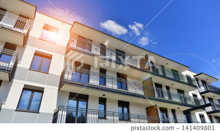 Contemporary urban apartment block with protruding balconies, white and grey facade contrast and reflective windows under a bright sky. Contemporary urban apartment block with protruding balconies, white and grey facade contrast and reflective windows under a bright sky. 141409801