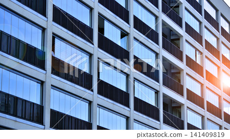 Contemporary urban apartment block with protruding balconies, white and grey facade contrast and reflective windows under a bright sky. Contemporary urban apartment block with protruding balconies, white and grey facade contrast and reflective windows under a bright sky. 141409819