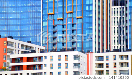 A low-rise residential building stands against a backdrop of tall glass buildings. An urban quarter of modern architecture. A low-rise residential building stands against a backdrop of tall glass buildings. An urban quarter of modern architecture. 141410290