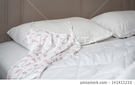 Floral nightdress on white bed in cozy modern bedroom Floral nightdress on white bed in cozy modern bedroom 141411218