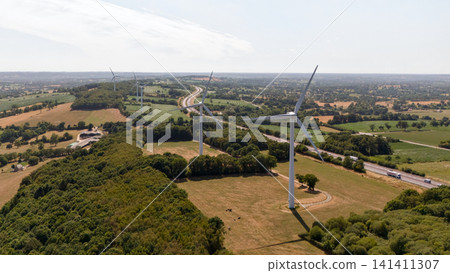 Two Wind Turbines Standing Together in Farmland Near Woodland 141411307