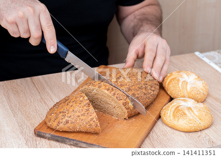 A man with a knife cuts bread on a wooden board. French baguettes. Different breeds on wooden background. 141411351