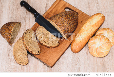 Different breeds on wooden background. Knife on a wooden board with bread and different buns on the table. Different breeds on wooden background. Knife on a wooden board with bread and different buns on the table. 141411353