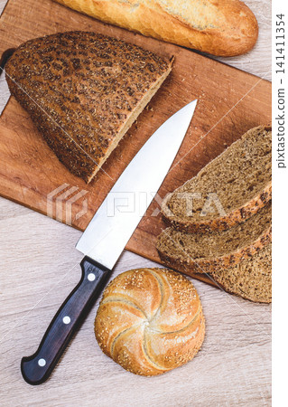 Different breeds on wooden background. Knife on a wooden board with bread and different buns on the table Different breeds on wooden background. Knife on a wooden board with bread and different buns on the table 141411354