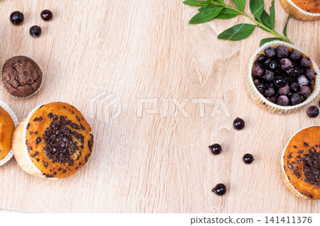 Chocolate muffin and nut muffin, homemade bakery on dark background. Muffin with blueberries on a wooden table. Fresh berries and sweet pastries on the board. Chocolate muffin and nut muffin, homemade bakery on dark background. Muffin with blueberries on a wooden table. Fresh berries and sweet pastries on the board. 141411376