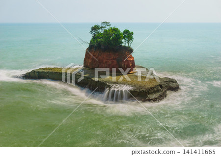 Aerial view of coastal rock formations rising from the sea with crashing waves and sandy beach in Indonesia Aerial view of coastal rock formations rising from the sea with crashing waves and sandy beach in Indonesia 141411665