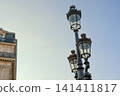 Ornate Parisian street lamp contrasting with a classic Haussmann building under a clear blue sky, travel destination 141411817