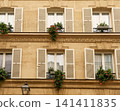 Classic Paris Haussmann style building facade showing traditional windows, shutters, and balconies adorned with vibrant flowers 141411835