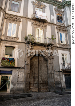 Naples, italy. December 30, 2024. Historic building facade in old town naples, italy, featuring a grand carved wooden door, balconies, and architectural details 141411890