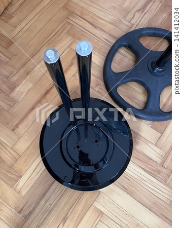 Weight plate and part of a gym bench resting on wooden floor Weight plate and part of a gym bench resting on wooden floor 141412034