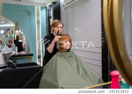 Young female hairdresser stylist working with scissors in beauty salon Stock Photo Young female hairdresser stylist working with scissors in beauty salon Stock Photo 141412652
