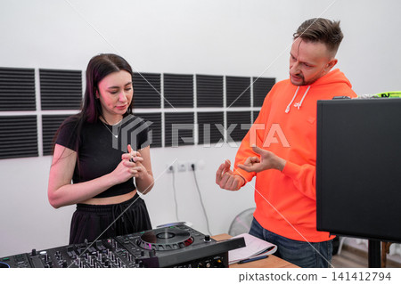 Man and woman in music studio reviewing DJ mixing notes and working with soundboards. DJ, music studio, notes, soundboard, review Man and woman in music studio reviewing DJ mixing notes and working with soundboards. DJ, music studio, notes, soundboard, review 141412794