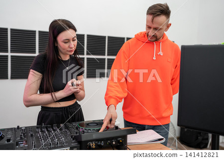 DJ teaches music mixing on professional equipment with young woman in recording studio. DJ, music mixing, studio, equipment, teaching DJ teaches music mixing on professional equipment with young woman in recording studio. DJ, music mixing, studio, equipment, teaching 141412821
