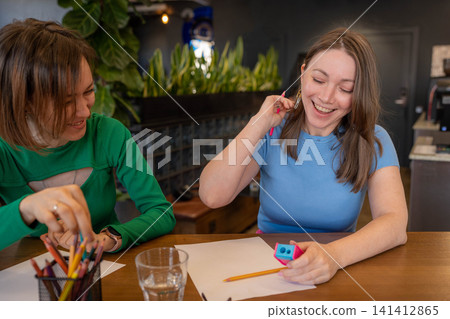 Women laughing and doodling at cafe table in cheerful friendly team building atmosphere. Laughing, doodling, cafe, team building, friendly. Women laughing and doodling at cafe table in cheerful friendly team building atmosphere. Laughing, doodling, cafe, team building, friendly. 141412865