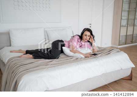 Happy woman relaxing on bed, looking smartphone screen early morning closeup. Smiling lady reading cellphone message lying in cozy bed. Positive brunette enjoy online communication in bedroom. Happy woman relaxing on bed, looking smartphone screen early morning closeup. Smiling lady reading cellphone message lying in cozy bed. Positive brunette enjoy online communication in bedroom. 141412894