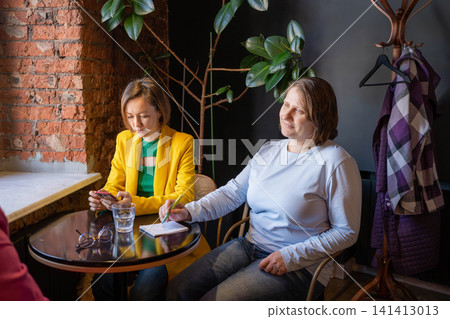 Women at round cafe table by brick wall having a friendly chat over coffee. Cafe, women, coffee, chat, brick wall. Women at round cafe table by brick wall having a friendly chat over coffee. Cafe, women, coffee, chat, brick wall. 141413013