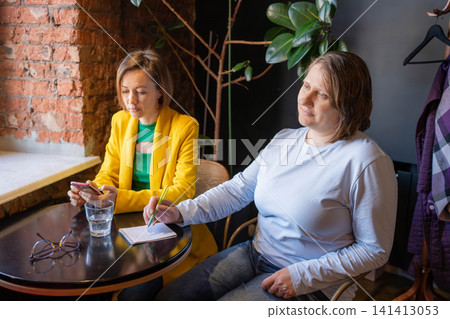 Smiling women at a cozy cafe sharing stories and laughter during a daylight meeting. Cafe, smiling, stories, laughter, daylight. Smiling women at a cozy cafe sharing stories and laughter during a daylight meeting. Cafe, smiling, stories, laughter, daylight. 141413053