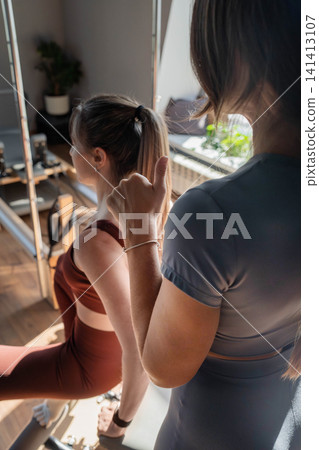 Foot work and core exercise on a Pilates Reformer machine illuminated by sunlight. Fit, healthy and strong authentical body. Fitness concept. Foot work and core exercise on a Pilates Reformer machine illuminated by sunlight. Fit, healthy and strong authentical body. Fitness concept. 141413107