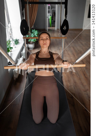 Elegant pilates pair performing synchronized deep stretches using reformer beds in bright wood-floored studio. Synchronized, deep stretch, reformer, studio, wood floor 141413120