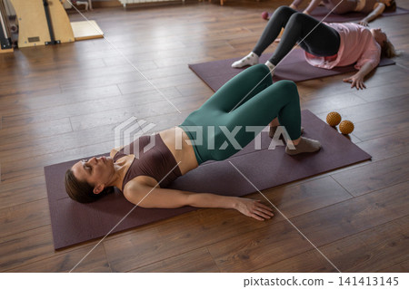 Glute bridge in Pilates workout. Active lifestyle and wellness concept. Stretch on mat in comfy clothes for flexibility and muscle health Glute bridge in Pilates workout. Active lifestyle and wellness concept. Stretch on mat in comfy clothes for flexibility and muscle health 141413145