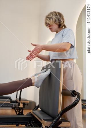 Woman training pilates with trainer on the reformer bed. Reformer pilates studio machine for fitness workouts in gym. Fit, healthy and strong authentical body. Fitness Woman training pilates with trainer on the reformer bed. Reformer pilates studio machine for fitness workouts in gym. Fit, healthy and strong authentical body. Fitness 141413174
